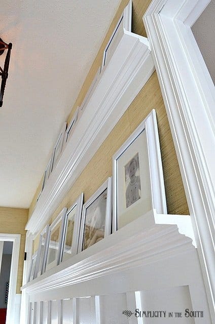 Need ideas for decorating your outdated hallway on a budget? This hallway was given board and batten wainscoting, DIY gallery wall shelves, new carriage style lighting, a DIY decorative air return cover and grasscloth