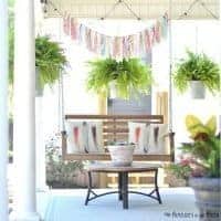 Summer front porch decorating ideas- Porch swing with rag and ribbon bunting and hanging pots with ferns in galvanized buckets